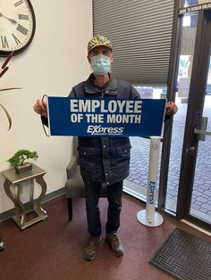 a man wearing a face mask holding a sign that reads employee of the month express