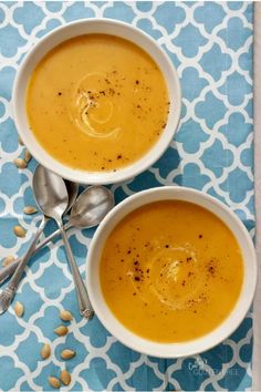 two white bowls filled with soup on top of a blue and white table cloth next to silver spoons