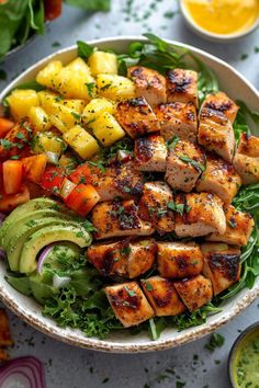 a bowl filled with chicken, avocado and pineapple slices on top of lettuce