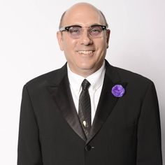 a man in a black suit and tie with a purple flower on his lapel