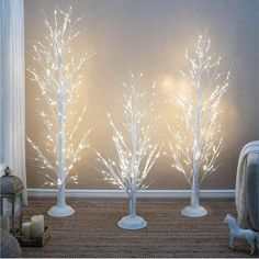 three white lighted trees in front of a gray wall