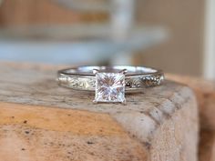 a white gold ring with a princess cut diamond in the center and filigree band