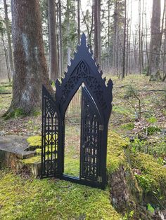 a black gate in the middle of a forest with moss growing on it's sides