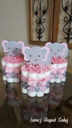 three elephant cupcakes with pink and grey bows on them sitting on a table