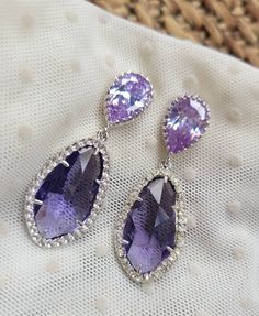 two pairs of earrings with purple stones and diamonds on top of a white cloth bag