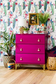 a bright pink dresser in the corner of a room with wallpaper and potted plants