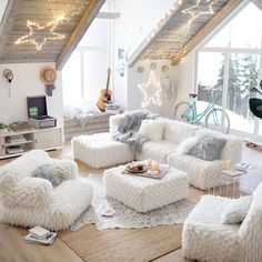 a living room filled with lots of white furniture and lights hanging from the rafters