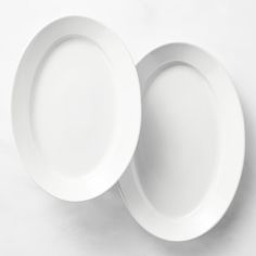 two empty white plates sitting on top of each other in front of a white background