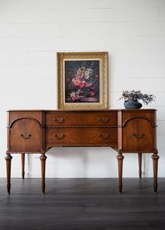 a painting on the wall next to a wooden dresser with drawers and two vases