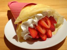 a pastry with whipped cream and strawberries in it on a white plate next to a pink cup