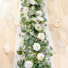 the table runner is decorated with white flowers and greenery