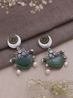 Dive into the realm of sophistication and charm with our Dual Tone Green Chandbali Earrings, a harmonious blend of tradition and contemporary flair. These earrings boast a graceful design adorned with exquisite half-moon detailing, showcasing the artisanal finesse that makes them a true embodiment of elegance. The dual tone green color palette imparts a refreshing and playful vibe, making them a versatile accessory that effortlessly transitions from day to night, from casual gatherings to festive celebrations. Meticulously crafted with precision, these earrings not only serve as a visual delight but also symbolize a timeless statement piece. Elevate your style effortlessly as you embrace the fusion of classic and modern aesthetics, allowing these Dual Tone Green Chandbali Earrings to becom Luxury Green Chandbali Jhumkas, Fusion Style Chandbali Brass Jhumkas, Silver Meenakari Chandelier Earrings For Festivals, Fusion Style Chandbali Jewelry With Oxidized Finish, Bohemian Kundan Chandbalis With Intricate Design, Festive Bollywood Chandbalis In Brass, Silver Dual-tone Chandbali Earrings, Dual-tone Chandbali Jewelry For Festive Season, Festive Brass Chandbalis With Matching Earrings