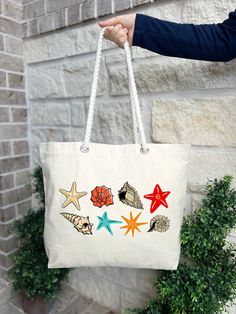 a person holding a white bag with starfishs and seashells on it