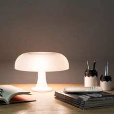 a table lamp sitting on top of a wooden table next to an open book and pencils