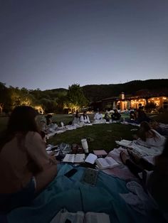 people are sitting on the grass reading books at night in front of a building with lights