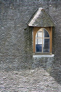 a window on the side of a building with a roof made of bricks and shingles