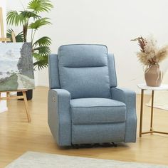 a blue recliner chair sitting on top of a hard wood floor next to a potted plant