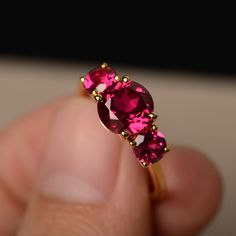 a close up of a person's hand holding a ring with two pink stones