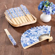 a blue and white plate, fan, vase with flowers on wooden table