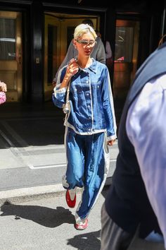 a woman walking down the street with a blue jean jacket and red shoes on her feet