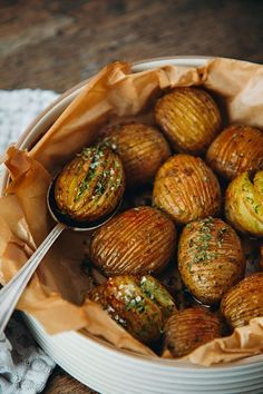 a bowl filled with cooked potatoes on top of a wooden table next to a fork