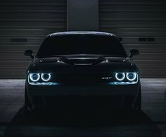 the front end of a black car with its lights on in a dark garage area