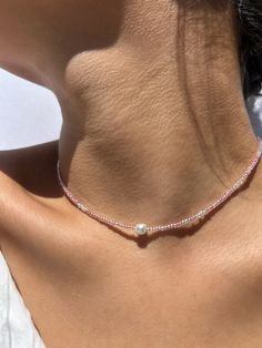 the back of a woman's neck wearing a necklace with a pearl on it