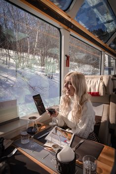 a woman sitting at a table in front of a window looking at her cell phone