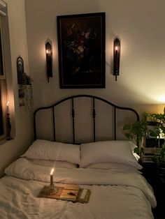 a lit candle is on the bed with white linens and pillows in front of a painting