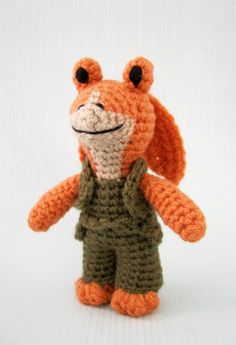 an orange crocheted stuffed animal wearing overalls and a green shirt with black eyes