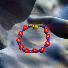 Red/Blue daisy chain bracelet with gold clasp. Red Flower Charm Jewelry For Spring, Red Jewelry With Flower Charm For Spring, Red Spring Jewelry With Flower Charm, Spring Red Jewelry With Flower Charm, Red Jewelry Spring Gift, Red Jewelry For Spring Gift, Red Flower-shaped Jewelry For Spring, Red Flower Jewelry For Spring, Red Flower-shaped Spring Jewelry