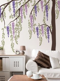 a white couch sitting under a tree with purple flowers on it's branches in front of a wall mural