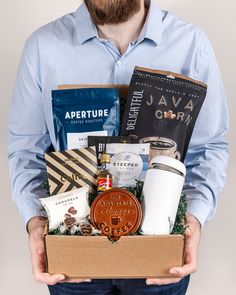 a man is holding a box filled with coffee, teas and other goodies