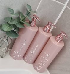 three pink soap dispensers sitting next to a green plant