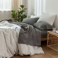 an unmade bed with grey and white linens in a small room next to a window