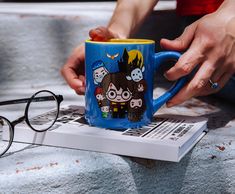 a person is holding a coffee mug with harry potter characters on it and reading glasses