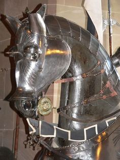 a large metal horse statue with armor on it's head and neck, standing in front of a brick wall