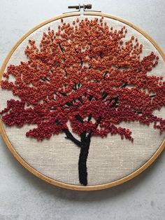 a red and black tree is embroidered on a white wall hanging from a wooden hoop