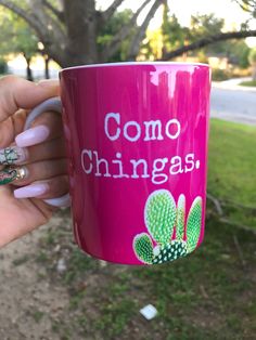 a woman holding a pink coffee mug with the words comoo chingas on it