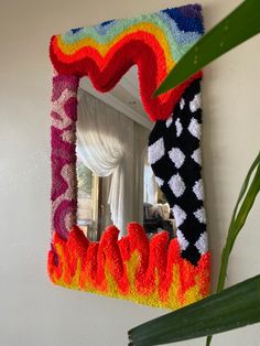 a colorful mirror hanging on the wall next to a plant