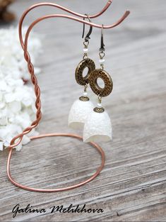 a pair of earrings is hanging from a wire on a wooden table with flowers in the background