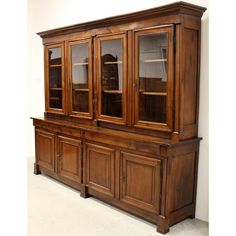 an old wooden china cabinet with glass doors and cupboards on the top, in front of a white wall