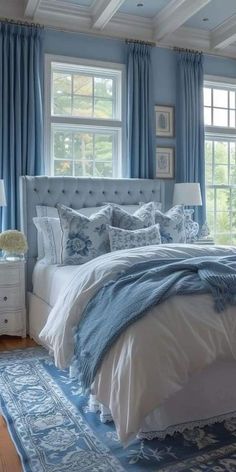 a bedroom with blue walls and white bedding, rugs on the floor and windows