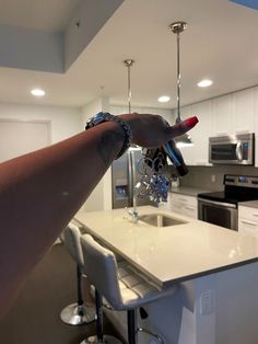 a woman's arm with bracelets hanging from the ceiling in a kitchen next to an island