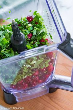 a blender filled with fresh vegetables on top of a wooden cutting board