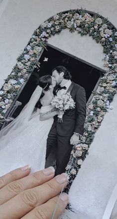 a wedding photo is being held in front of a frame with flowers and greenery