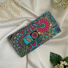 a colorful wallet sitting on top of a white cloth next to flowers and pearls,