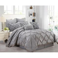 a bed with grey comforter and pillows in a room next to a white dresser