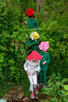 three children in green and red outfits standing on the ground with flowers around their heads