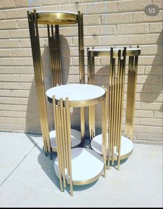 three gold and white side tables sitting next to each other on a sidewalk in front of a brick wall